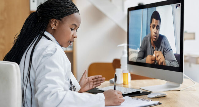 Shot of a young doctor writing notes during a video call with a patient on a computer